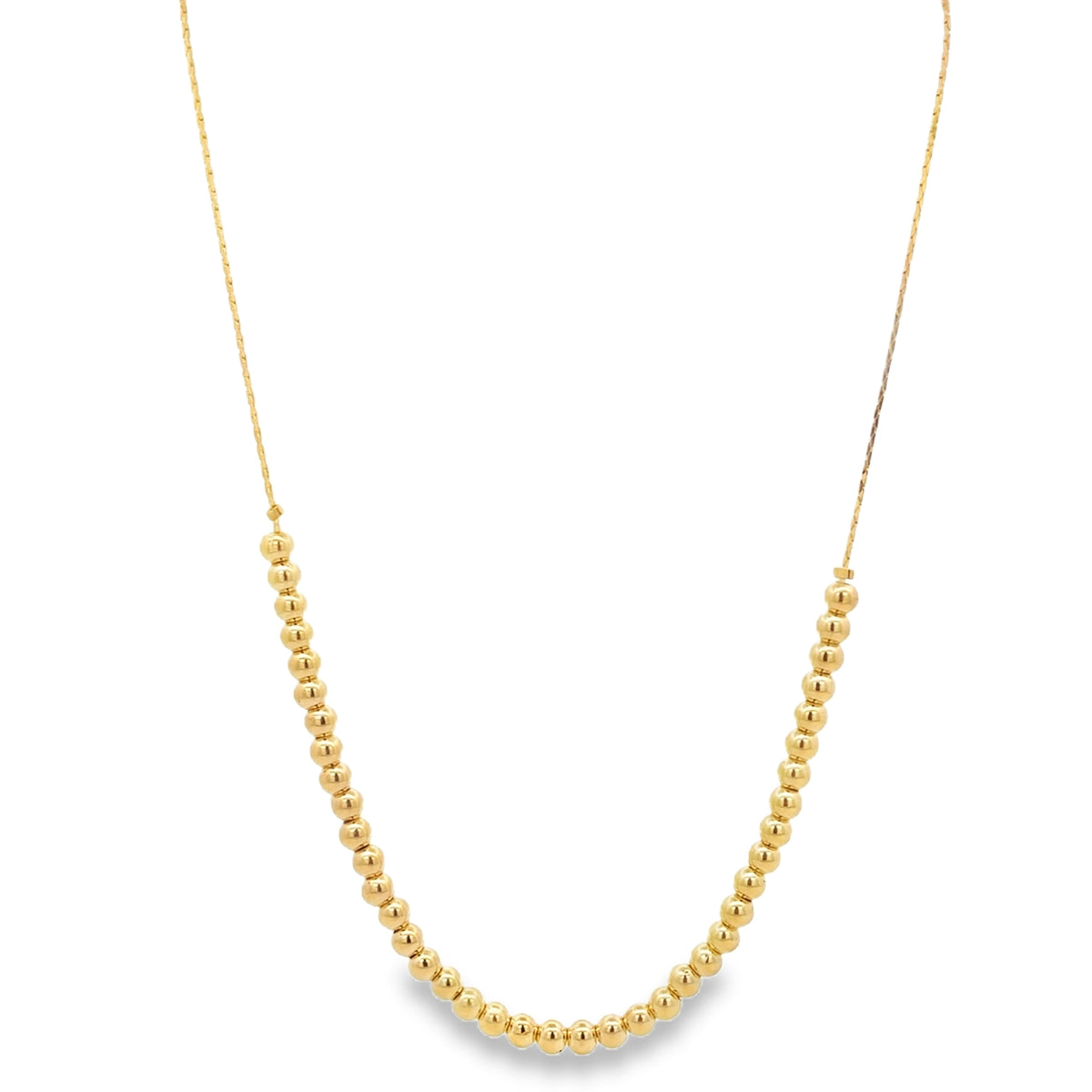 A delicate gold bead necklace hangs against a plain white background, displaying a curved strand of polished spherical charms.