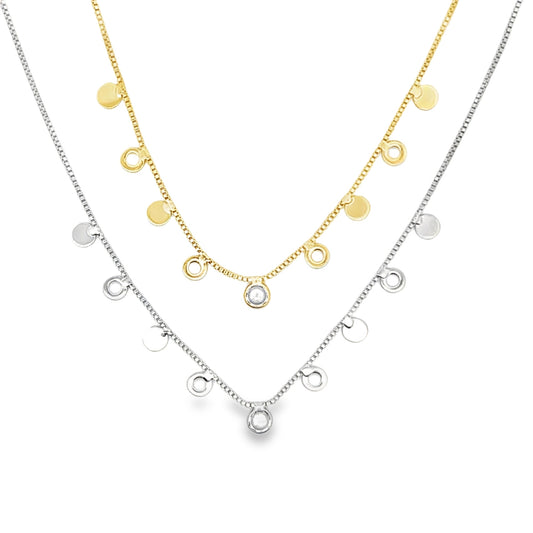 A gold necklace with coin charms and a silver necklace with charm drops are layered together against a white background.