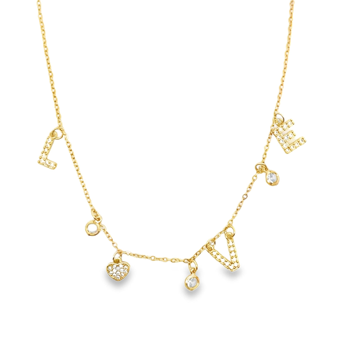 A delicate gold charm necklace sparkles against a white background, featuring pavé-set crystal charms that spell out "LOVE" alongside tiny hearts and round stones.