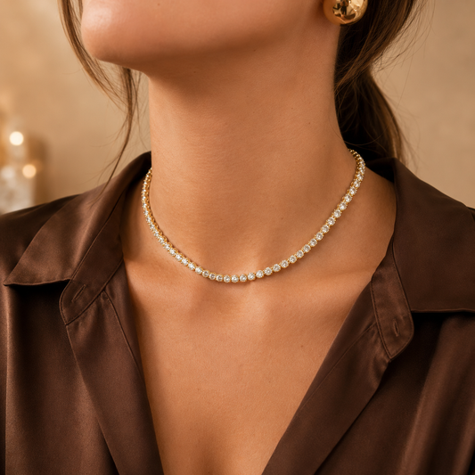 A woman wears a sparkling diamond tennis necklace with gold details paired with a brown silk blouse.