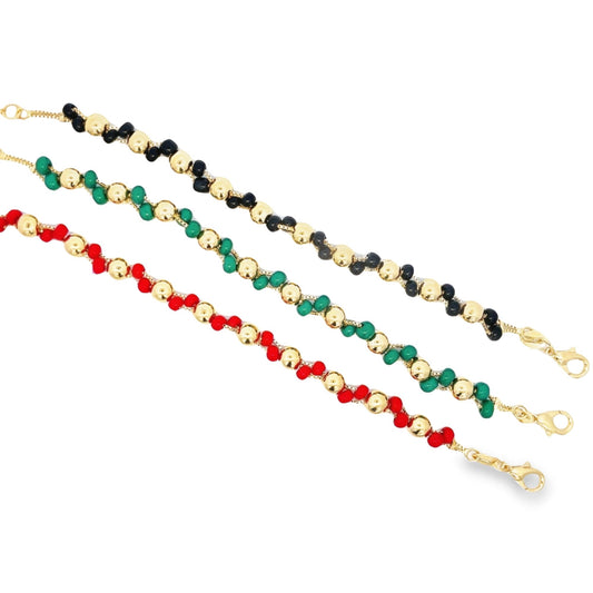 Three handmade bead bracelets featuring alternating gold beads with black, green, and red stones display their vibrant pan-African colors against a clean white background.