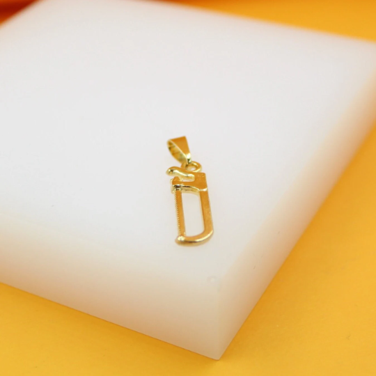 A shiny gold hacksaw pendant rests on a white display block.
