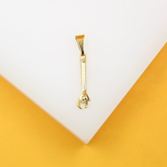 A small, polished gold wrench pendant rests centrally on a white display surface against a vibrant yellow background.
