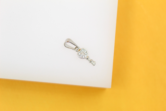 A sparkling silver heart-shaped key pendant rests on a white display against a vibrant yellow background.