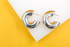 Two chunky silver hoop earrings rest neatly on a white and yellow display background.