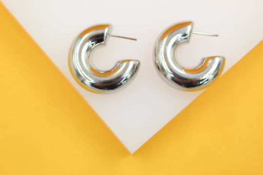 A pair of shiny silver chunky hoop earrings rest on a white and yellow display stand.
