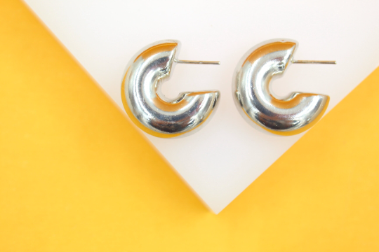 A pair of glossy silver hoop earrings rests on a white display against a vibrant yellow background.
