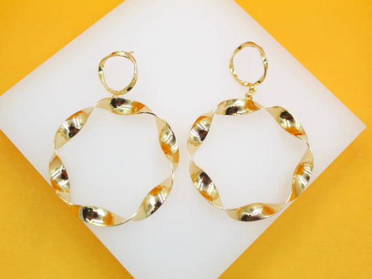 A pair of polished gold twist hoop earrings rests on a white display against a vibrant yellow background.