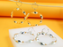 A pair of gold twisted hoop earrings hangs above matching silver earrings resting on a white display against a vibrant orange background.