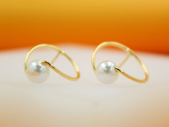 A pair of elegant gold-plated open hoop earrings features a single lustrous white pearl nestled along the curved wire design, resting against a soft-focus background.