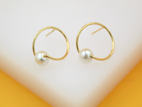 A pair of elegant gold hoop earrings featuring lustrous white pearls resting on a minimalist geometric design.