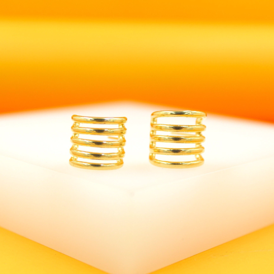 A pair of gold-plated multi-band ear cuffs rests on a white display against a warm orange background.