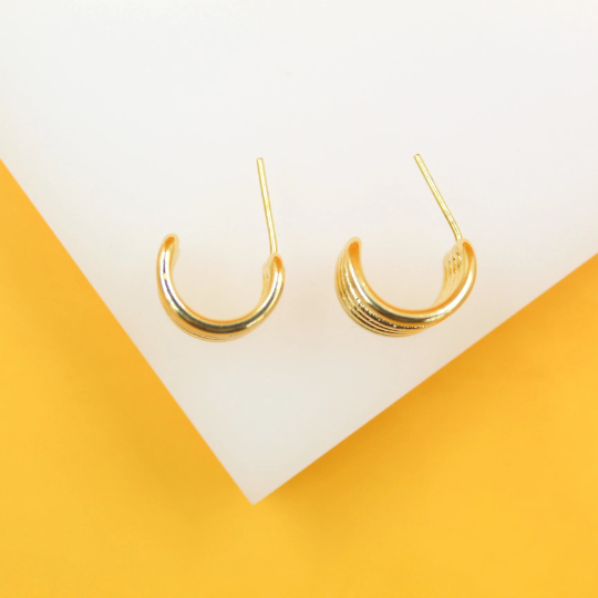 A pair of ribbed gold hoop earrings rests on a white display against a vibrant yellow background.