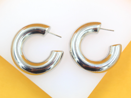 A pair of shiny silver chunky hoop earrings rest against a white and yellow surface.