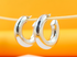 A pair of glossy silver chunky hoop earrings hangs delicately from a thin wooden stick against a warm orange background.