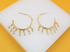 A pair of gold hoop earrings features hanging marquise-cut crystal charms against a white and yellow background.