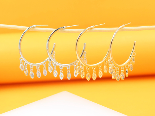 Four elegant hoop earrings with dangling marquise crystal charms hang in a row against a vibrant yellow backdrop.