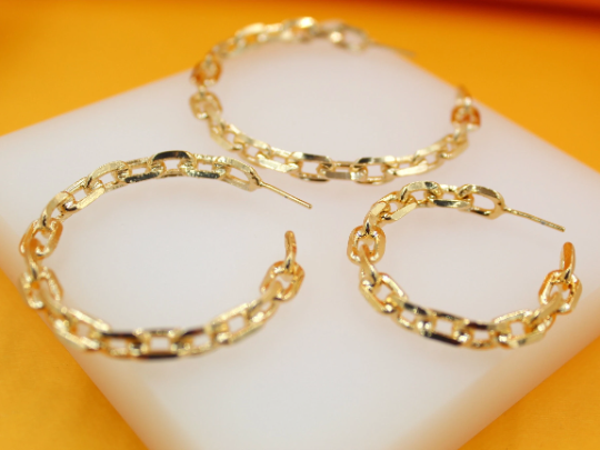 Three gold chain-link hoop earrings rest on a white display block against an orange background.