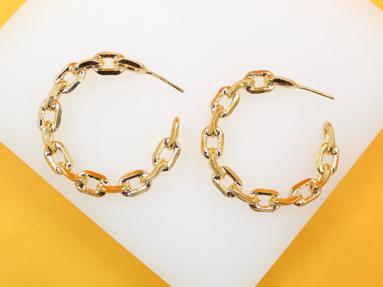 A pair of gold chain-link hoop earrings rests on a white display surface.