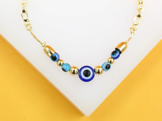 A delicate gold chain necklace features a central blue evil eye bead flanked by smaller glass evil eye beads and golden spheres.