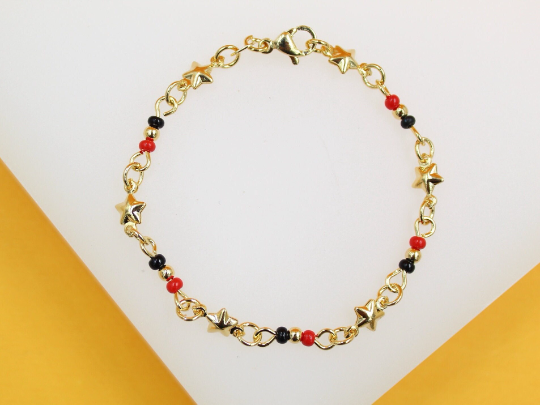 A gold link bracelet features alternating star charms and small black and red beads, displayed against a light-colored background.