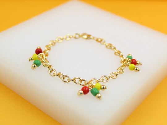 A delicate gold chain bracelet features colorful red, yellow, and green bead charms resting on a white display surface.