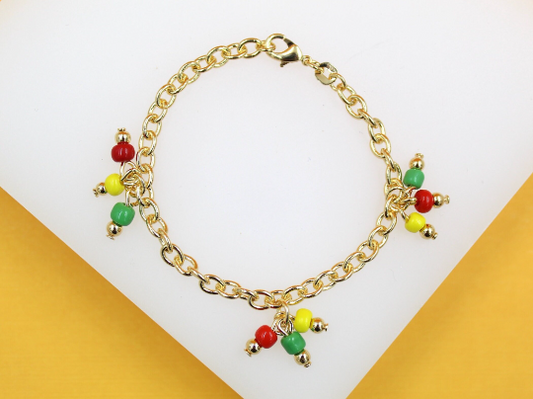 A delicate gold chain bracelet features dangling charms made of colorful red, yellow, and green beads against a neutral white and yellow background.