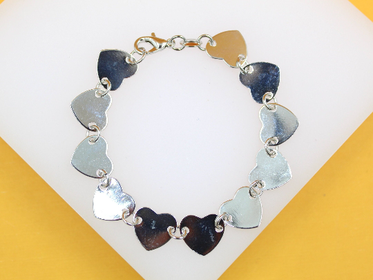 A silver heart charm bracelet rests on a white display surface against a warm yellow background.