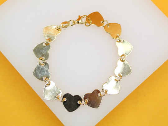 A charming gold-plated bracelet features a continuous chain of interlocking heart-shaped charms resting on a white display surface.