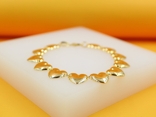 A delicate gold heart charm bracelet rests gracefully on a white display block.