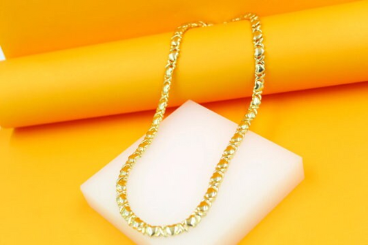 A gold hug and kiss XO link necklace rests gracefully on a white display block against a vibrant orange background.