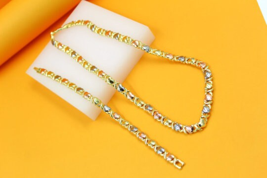 A tri-color gold necklace and matching bracelet rest elegantly on a white display against a vibrant orange background.