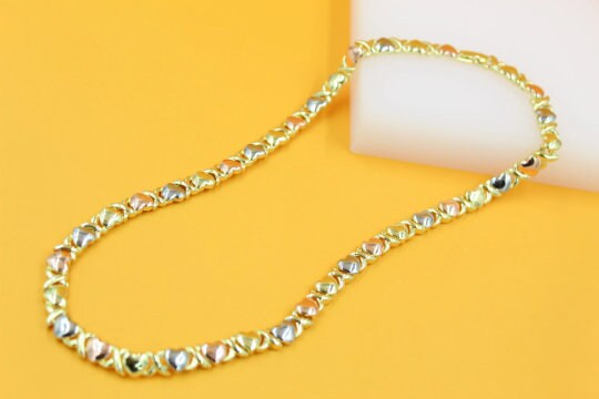 A tri-color gold hug and kiss bracelet rests against a warm yellow and white background.