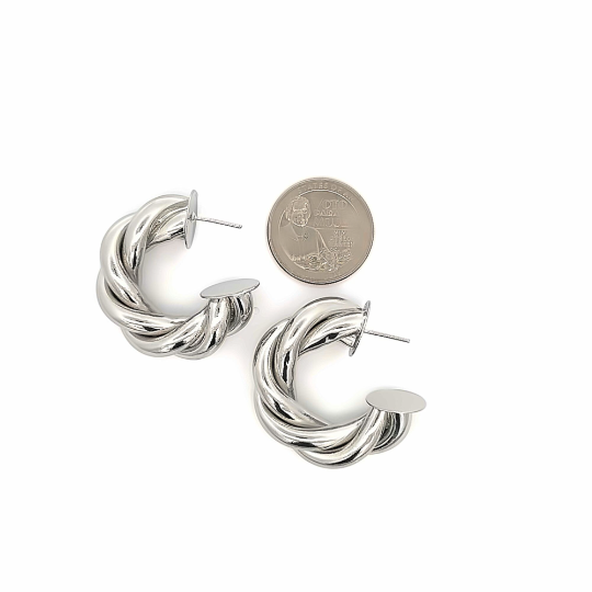 A pair of chunky silver twisted hoop earrings rests next to a US quarter on a white background for size comparison.