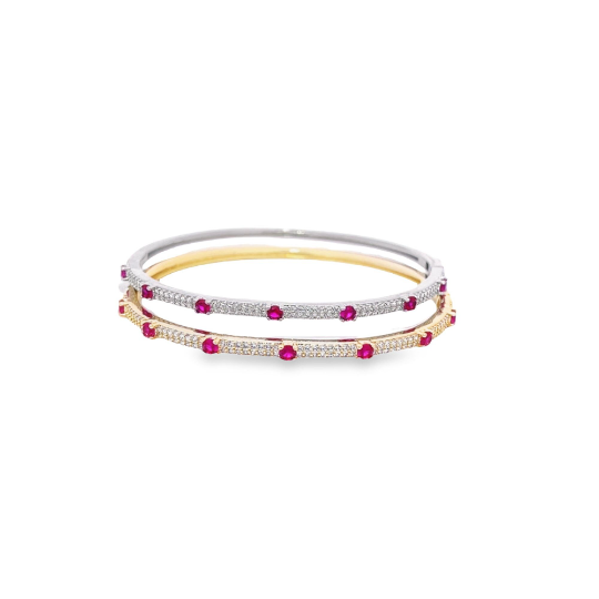 Two interlocking gold and silver bangles feature sparkling diamond pavé and vibrant ruby stones against a clean white background.