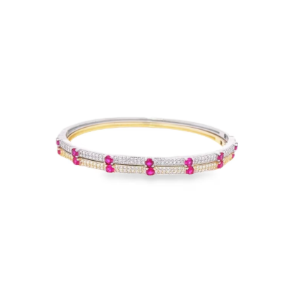A double-banded gold and silver diamond bangle bracelet sparkles against a white background, featuring vibrant red ruby accents.