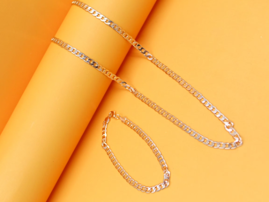 A shiny gold cuban link necklace and matching bracelet rest gracefully against a vibrant yellow cylindrical backdrop.