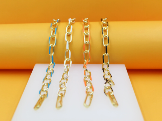 Four gold link chains featuring blue, white, orange, and black enamel details rest vertically against a vibrant yellow and white backdrop.