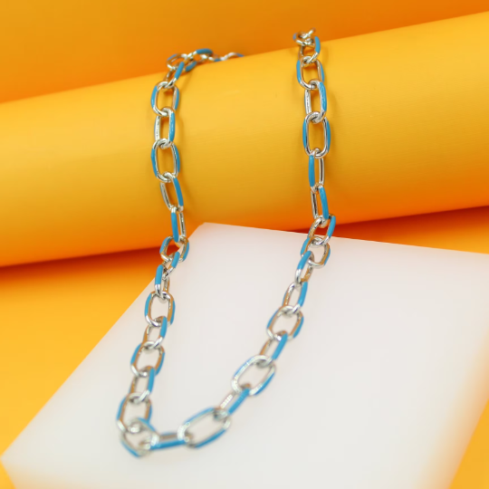 A chunky silver chain necklace featuring vibrant blue enamel links rests elegantly against a white display block with a bright yellow background.