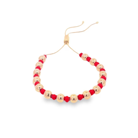 A handmade adjustable slider bracelet features alternating shiny gold metallic beads and vibrant red faceted beads on a fine cord.