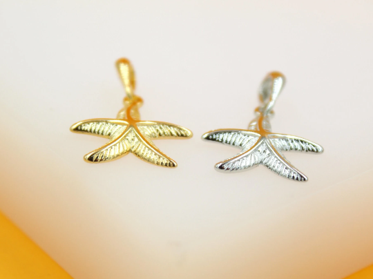 Two metallic starfish charms, one in gold and one in silver, rest side by side against a light background.