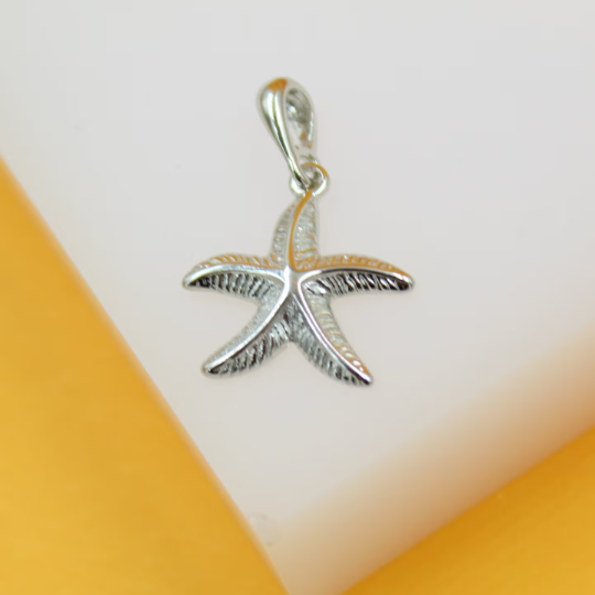 A detailed silver starfish pendant rests on a clean white display surface against a warm yellow backdrop.