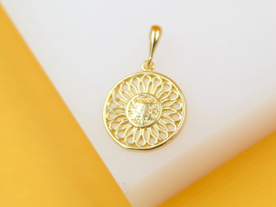 A gold-plated pendant featuring an intricate sunburst or flower petal design rests on a white and yellow surface.