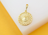 A gold-plated pendant featuring an intricate sunburst or flower petal design rests on a white and yellow surface.
