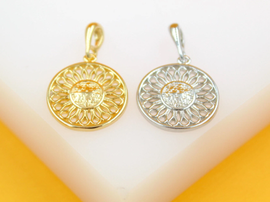 Two circular sunflower pendants, one in gold and one in silver, rest side-by-side on a white surface.