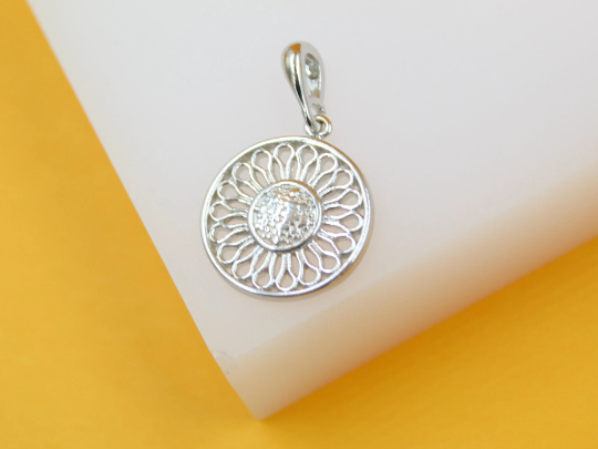 A silver sunflower pendant rests on a white display surface against a vibrant yellow background.