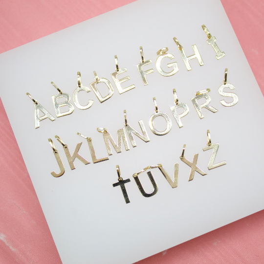 A collection of shiny gold alphabet letter pendants arranged neatly on a white display card.