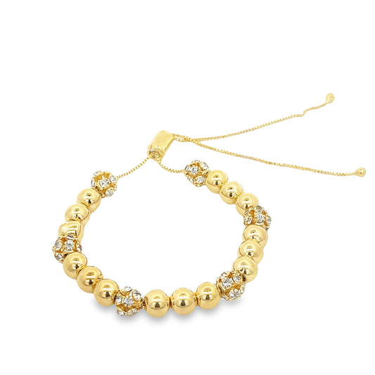 A gold bolo bracelet features alternating smooth metallic beads and sparkling rhinestone-encrusted spheres on an adjustable chain.