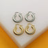 A pair of silver and a pair of gold twisted dome hoop earrings rest side by side on a white display stand.