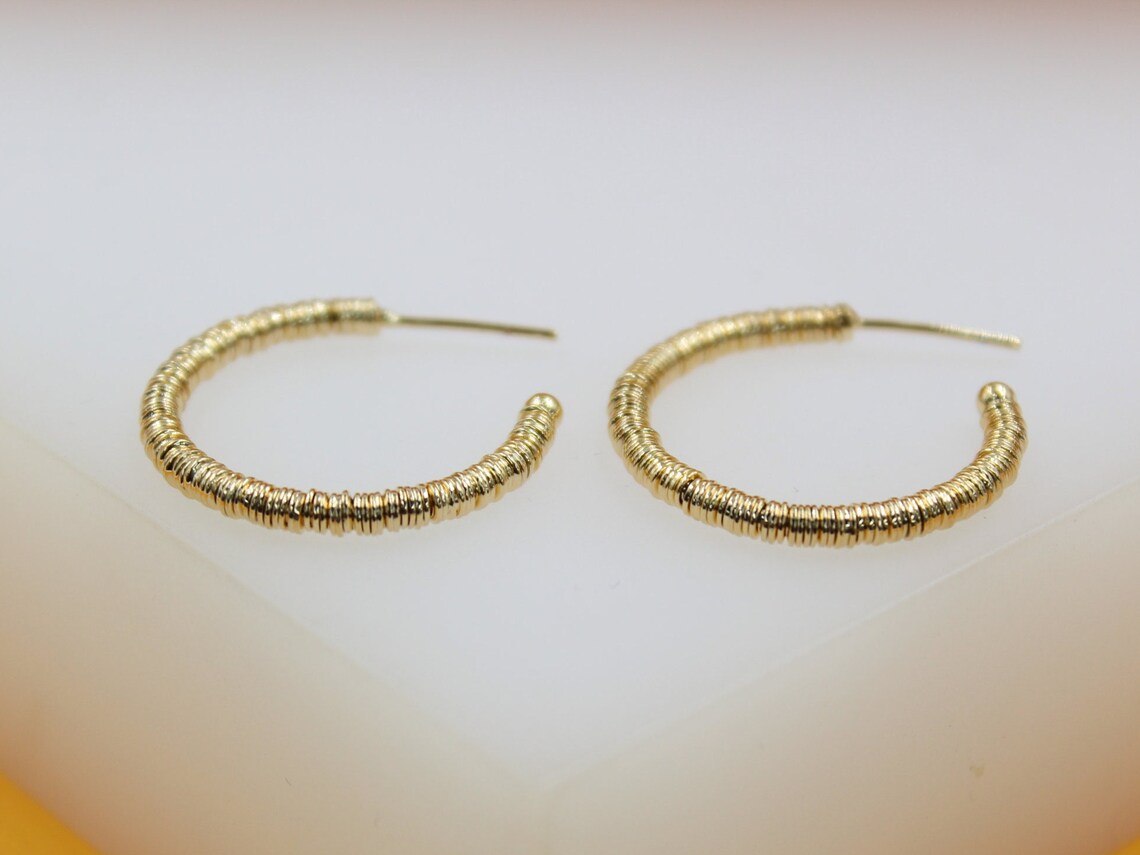 A pair of textured gold hoop earrings rests neatly on a light surface.